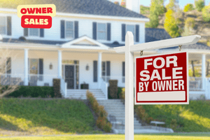 A white house in the USA for sale by the owner with a red for sale sign by the owner outside.